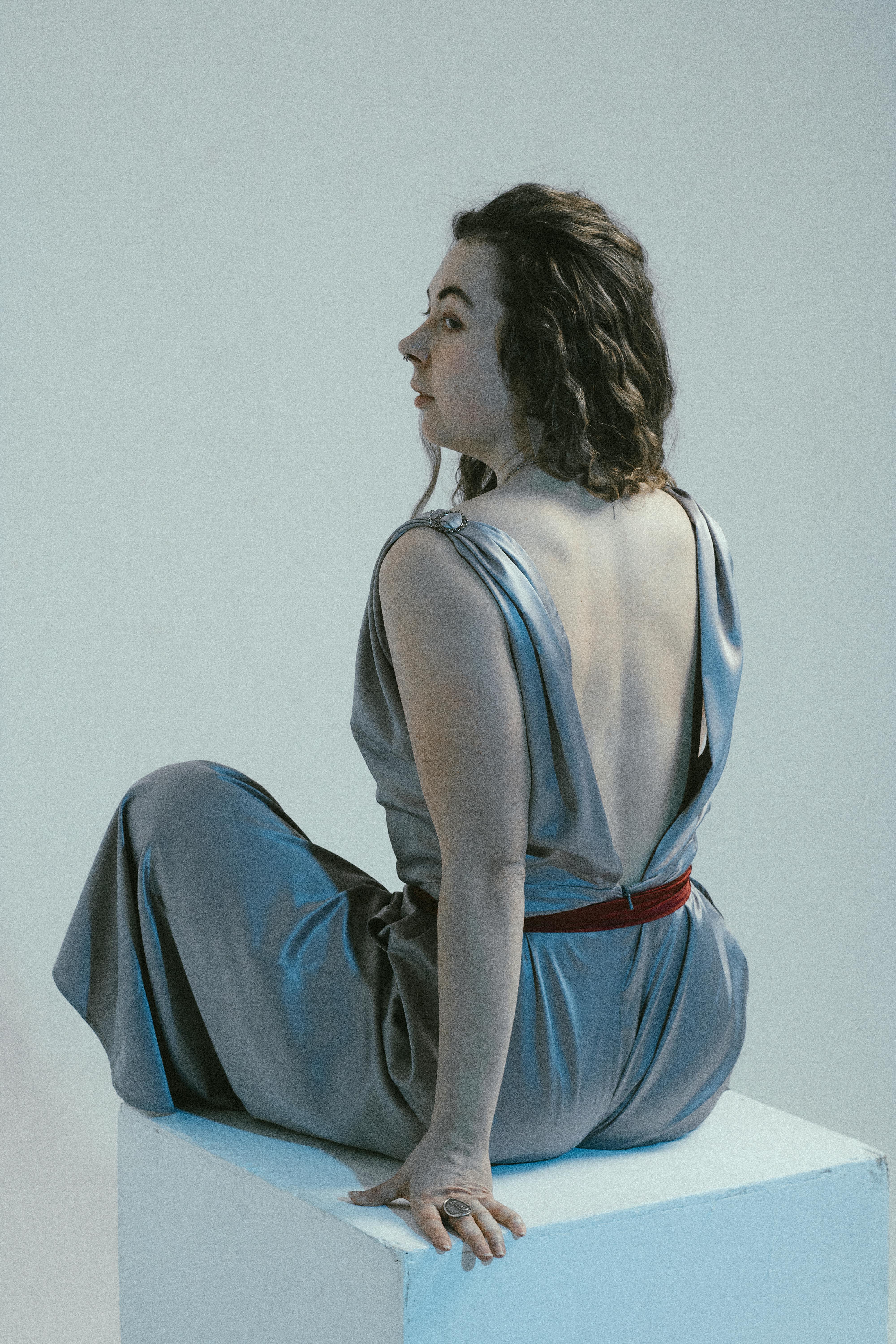 A woman in a stylish backless dress sitting gracefully in a studio setting.