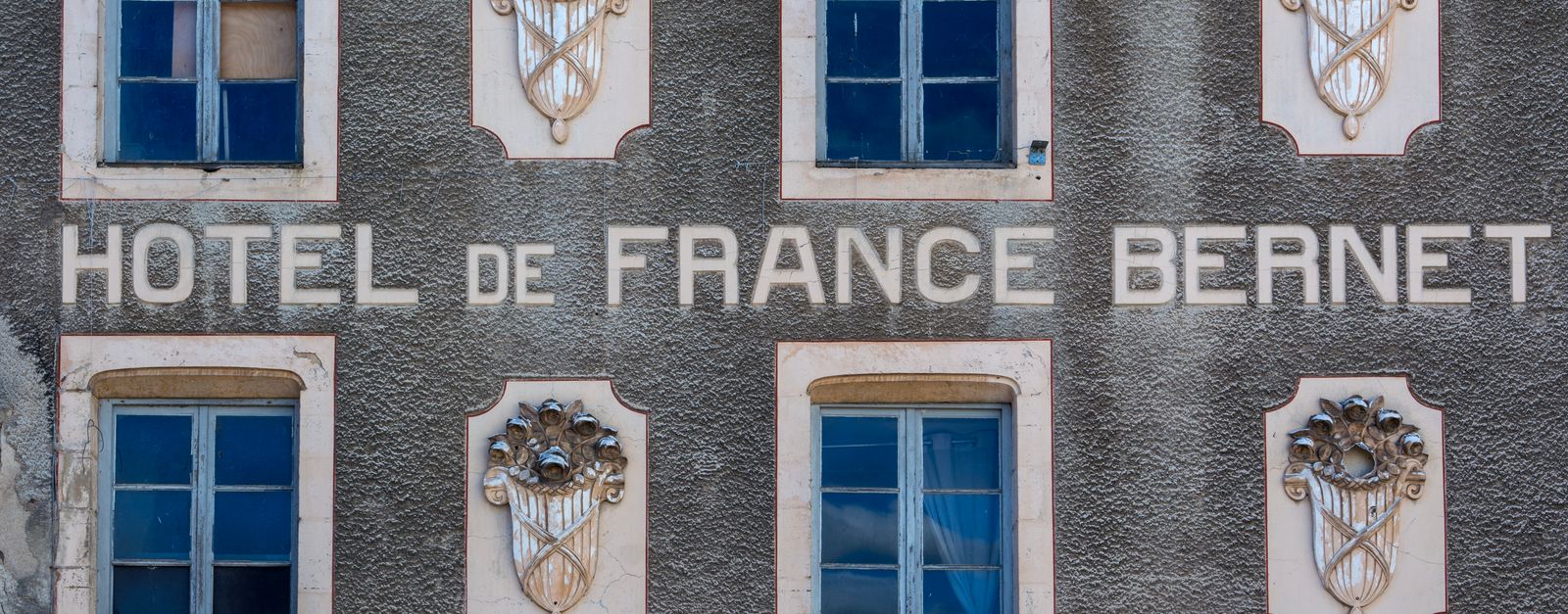Close-up of Hotel de France Bernet facade in Saint-Saulge, showcasing vintage windows and ornate design elements.