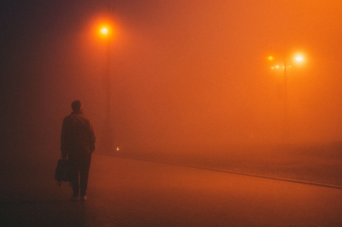 Silhouette of a man walking alone down a foggy, dimly lit city street at night, illustrative photo
