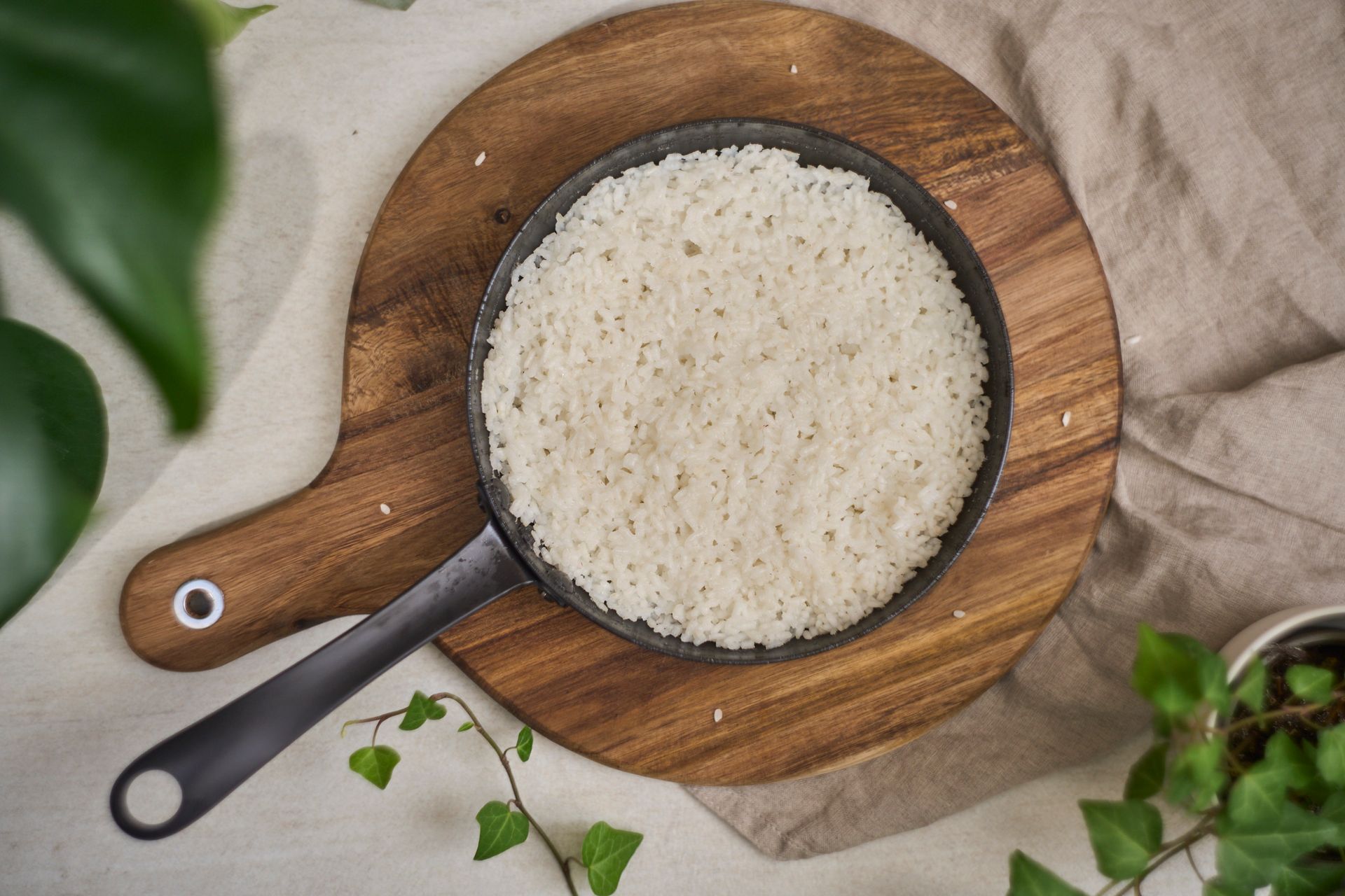 Top view of cooked rice in a frying pan on a wooden cutting board surrounded by greenery.
