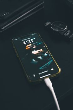 Smartphone charging on a dark wooden table with a digital watch nearby.. smartphone, charging, dark