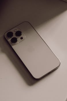 Close-up of a smartphone with three cameras on a neutral surface in soft lighting.
