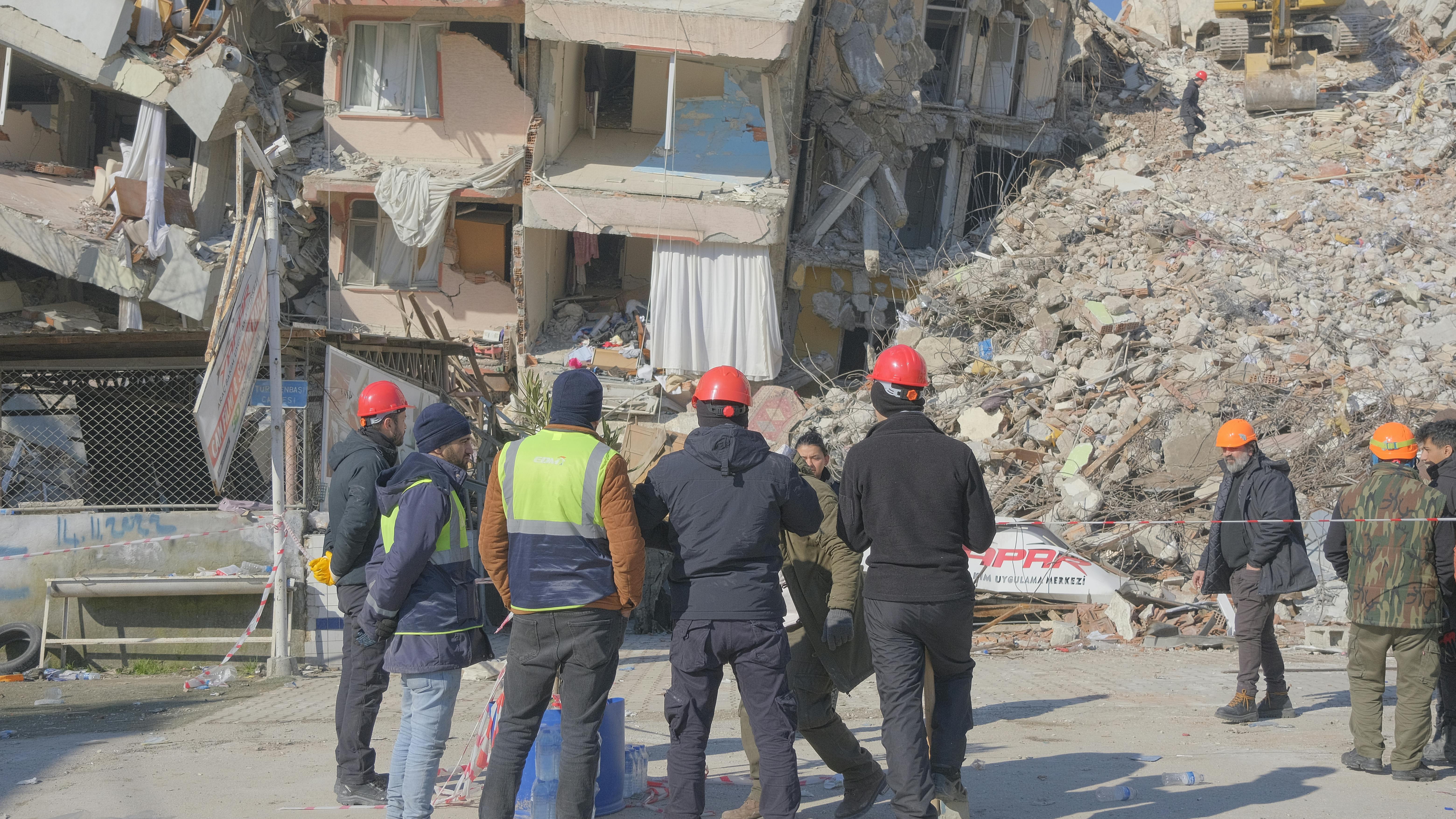 Emergency workers assess damage at an earthquake site with urban ruins.