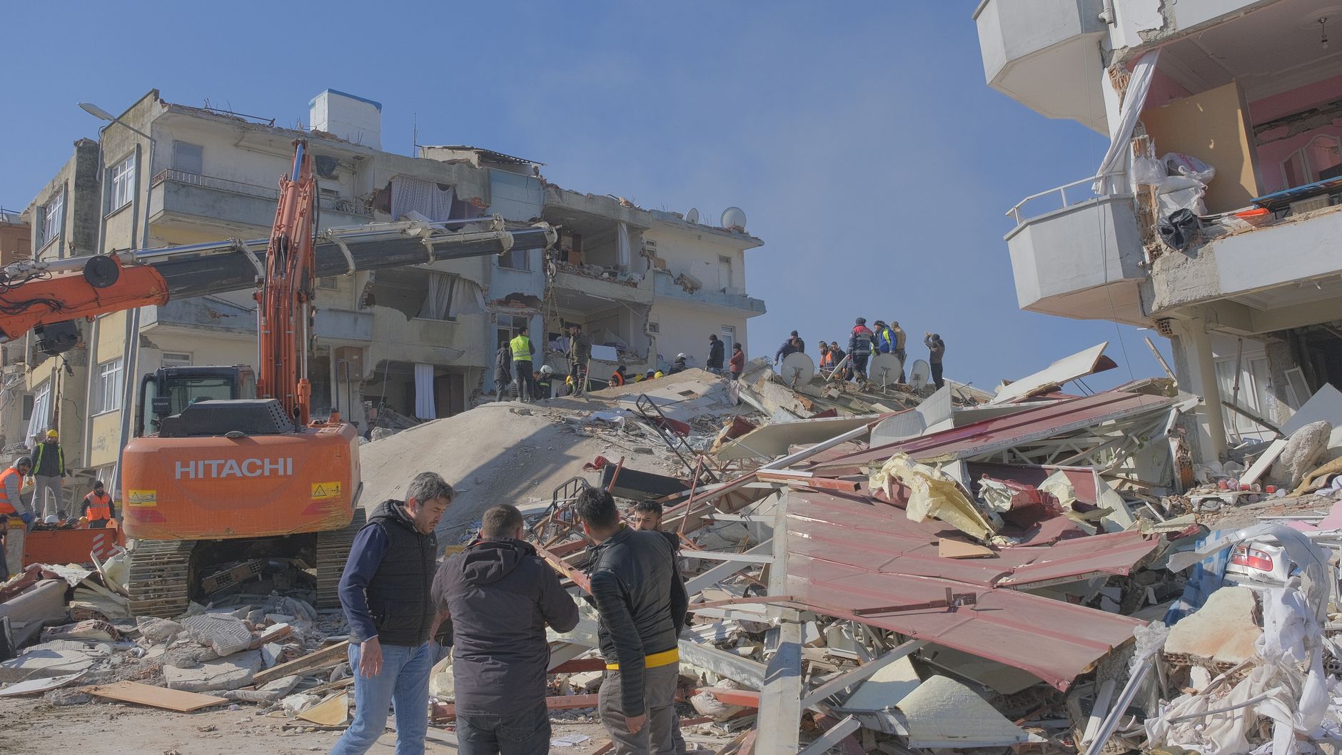 Rescue workers and machinery at an earthquake site showing damaged buildings and debris.