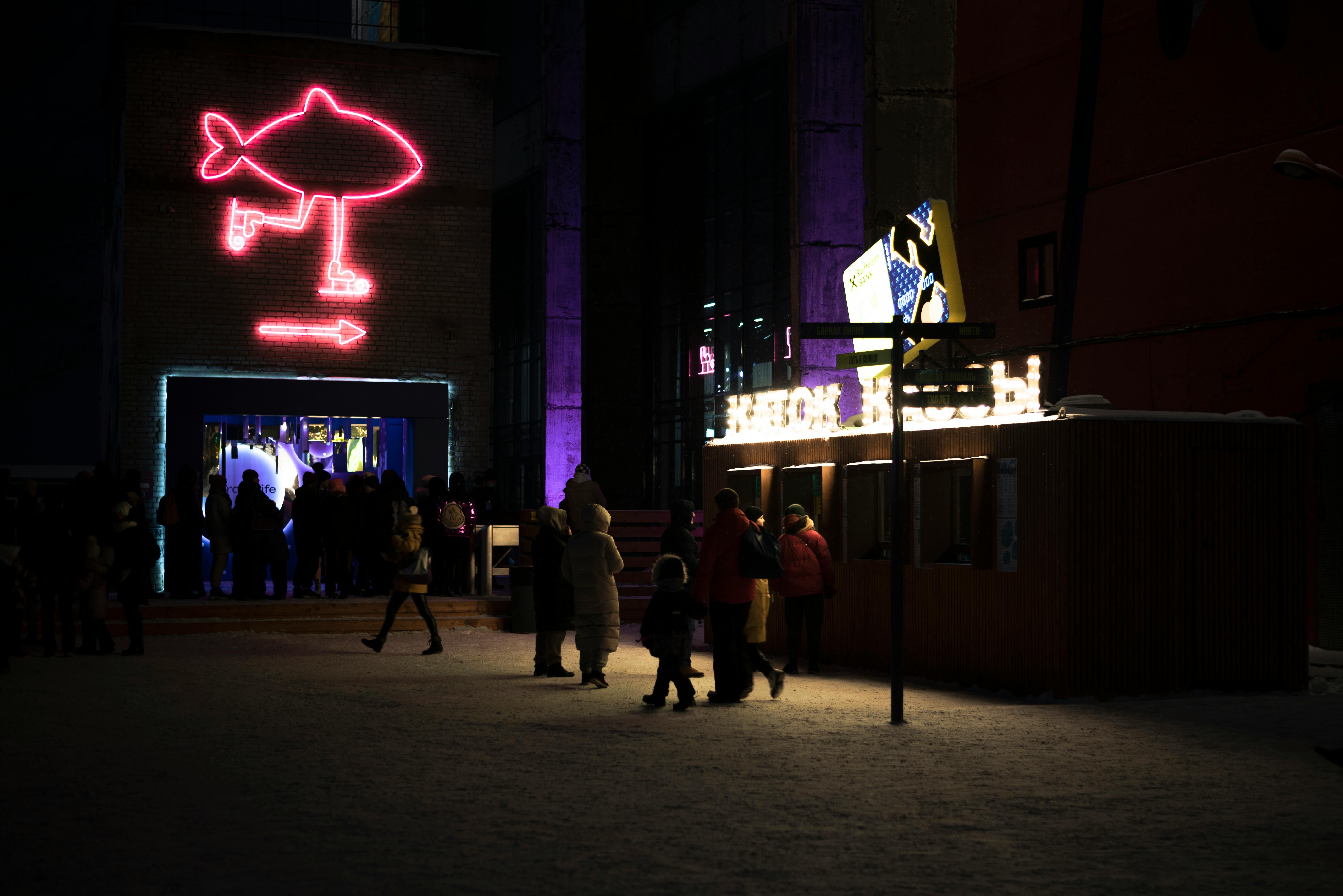 Free A lively urban winter night scene featuring a neon sign and people walking in a snowy setting. Stock Photo