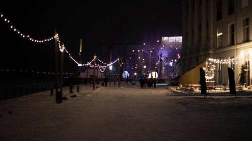 Free Snow-covered street adorned with festive lights at night, capturing a cozy winter ambiance. Stock Photo