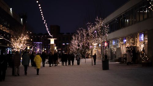 Free A lively urban street scene with Christmas lights, snowy paths, and people strolling. Stock Photo