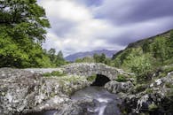 石桥横跨溪流，背景是郁郁葱葱的青山和山脉