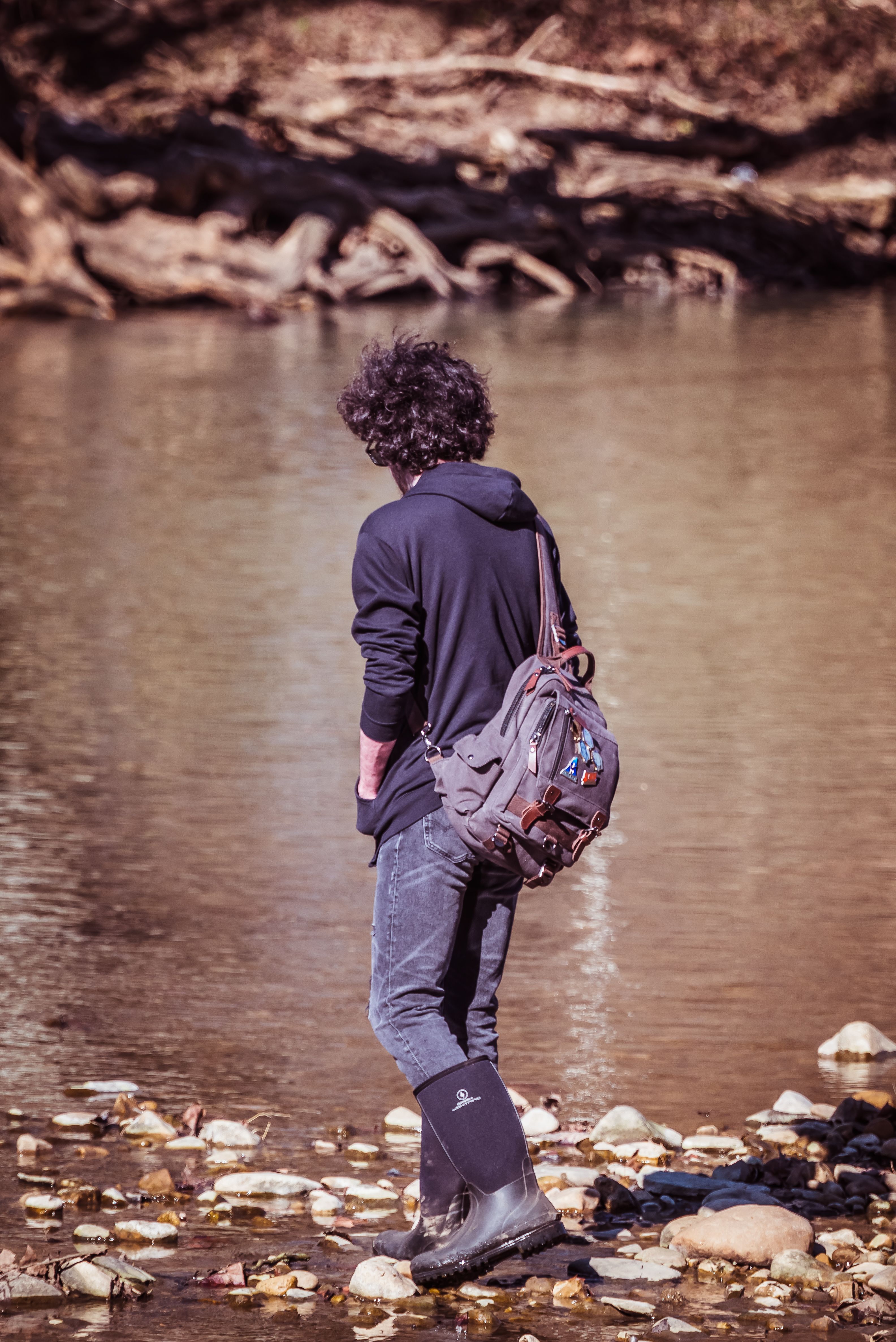 A young adult wearing a hoodie and backpack exploring a rocky riverbank, capturing the spirit of adventure.