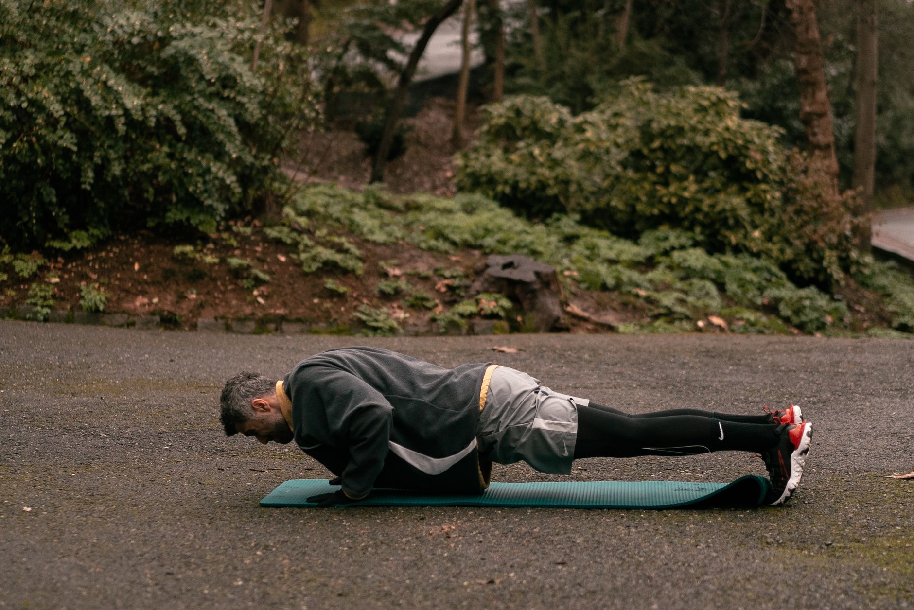 Man doing a plank on a yoga mat outdoors, focusing on fitness and strength training.