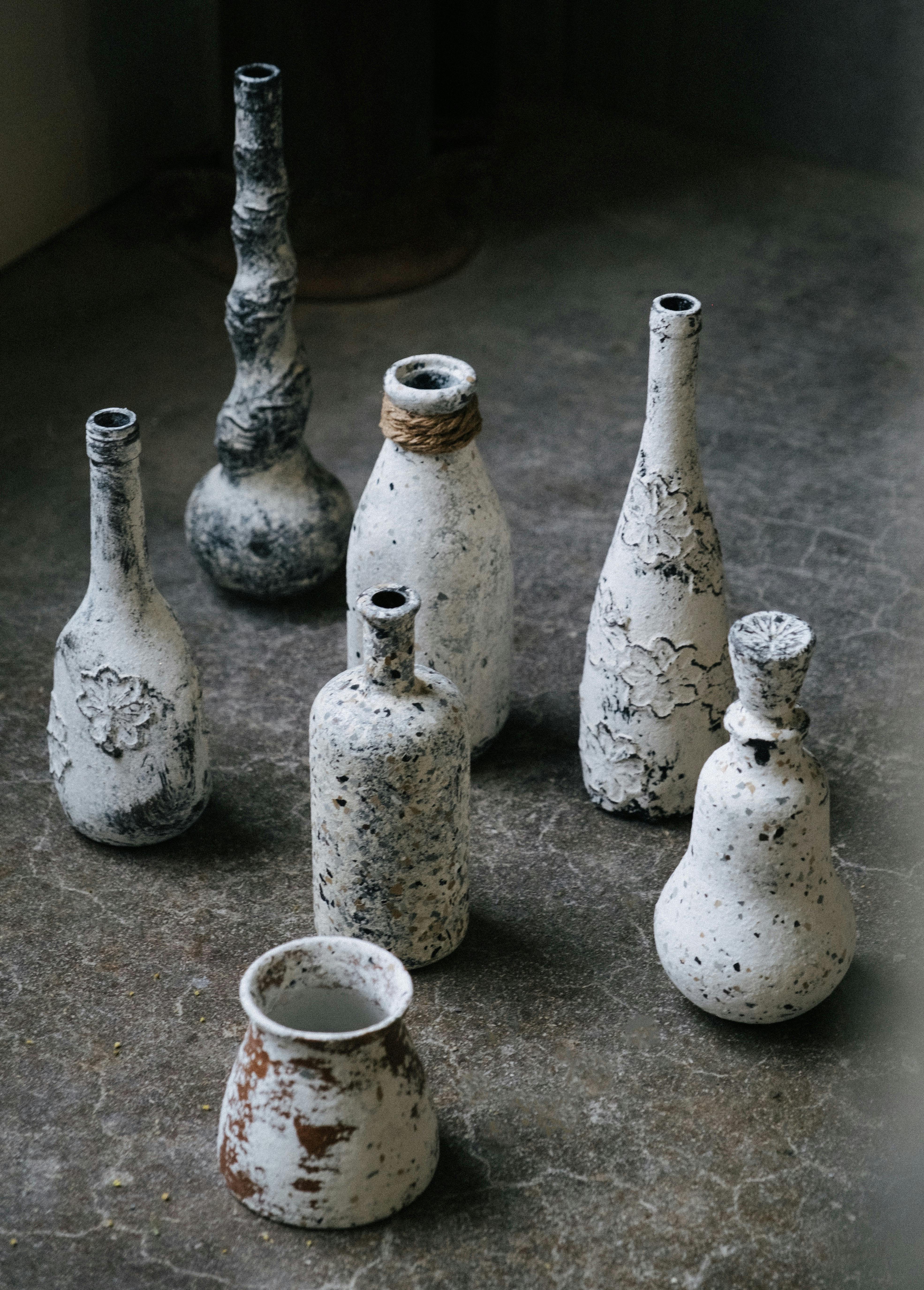 A collection of vintage ceramic vases with textured designs placed on a distressed stone surface, offering an artistic look.