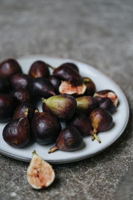 Ripe purple figs arranged on a marble plate, showcasing a rustic food photography style.