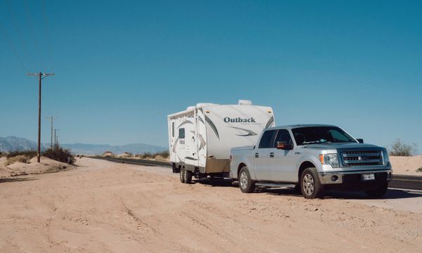 Trailer Hire โ Silver truck towing an Outback trailer on a desert road under clear blue skies.