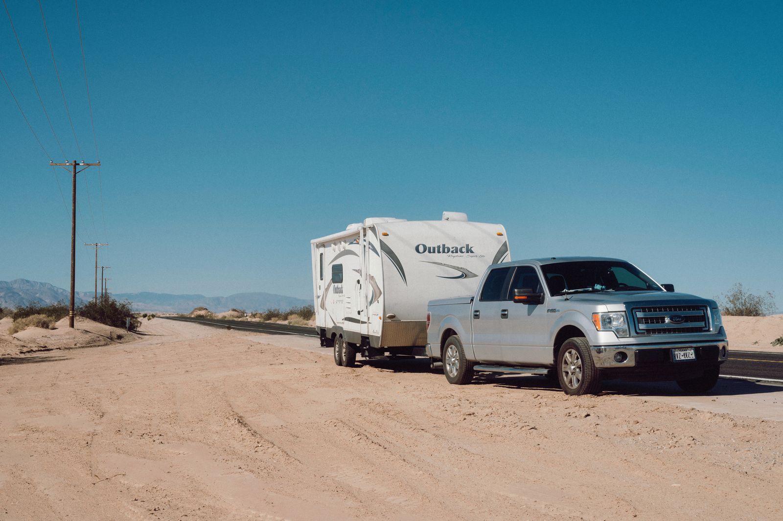 A truck towing a camping trailer on a desert highway, the kind of setup a trailer-rated backup camera system is built for