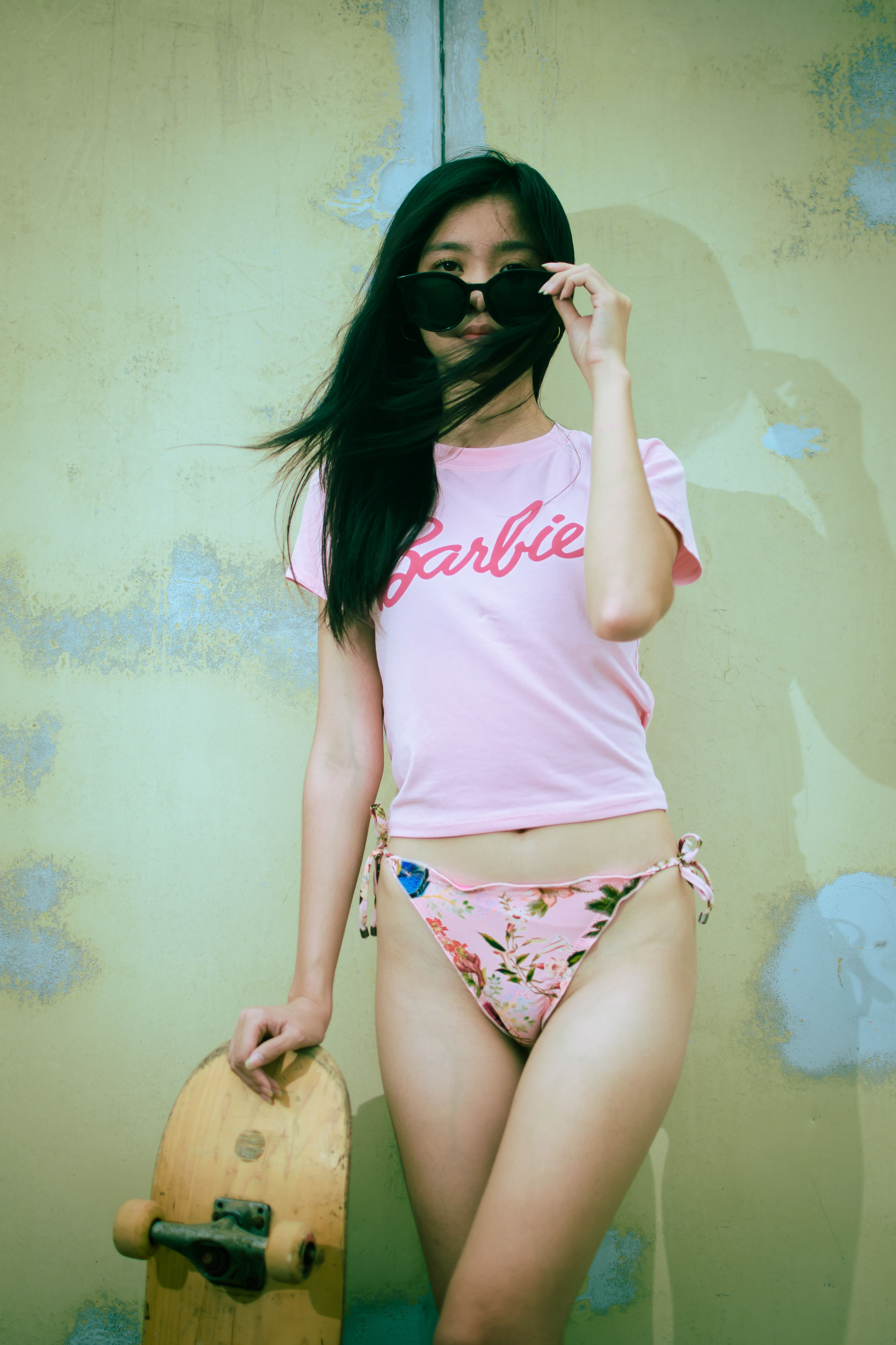Stylish young woman posing with a skateboard in summery attire, exuding a cool and trendy vibe.
