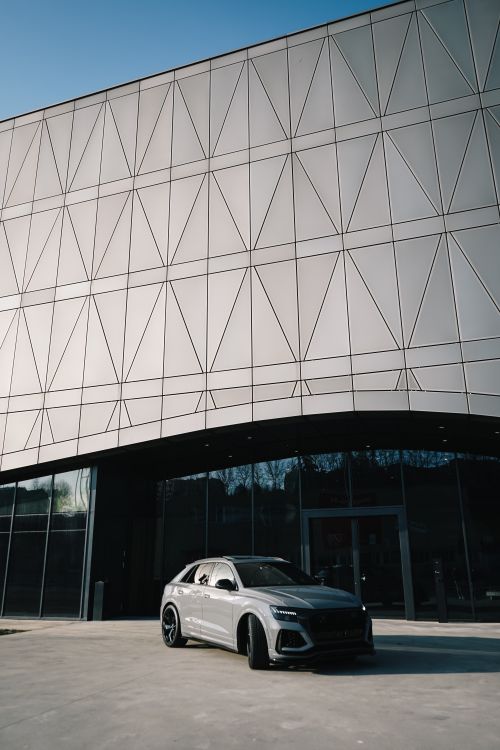 Free Sleek SUV parked in front of modern geometric building facade. Stock Photo