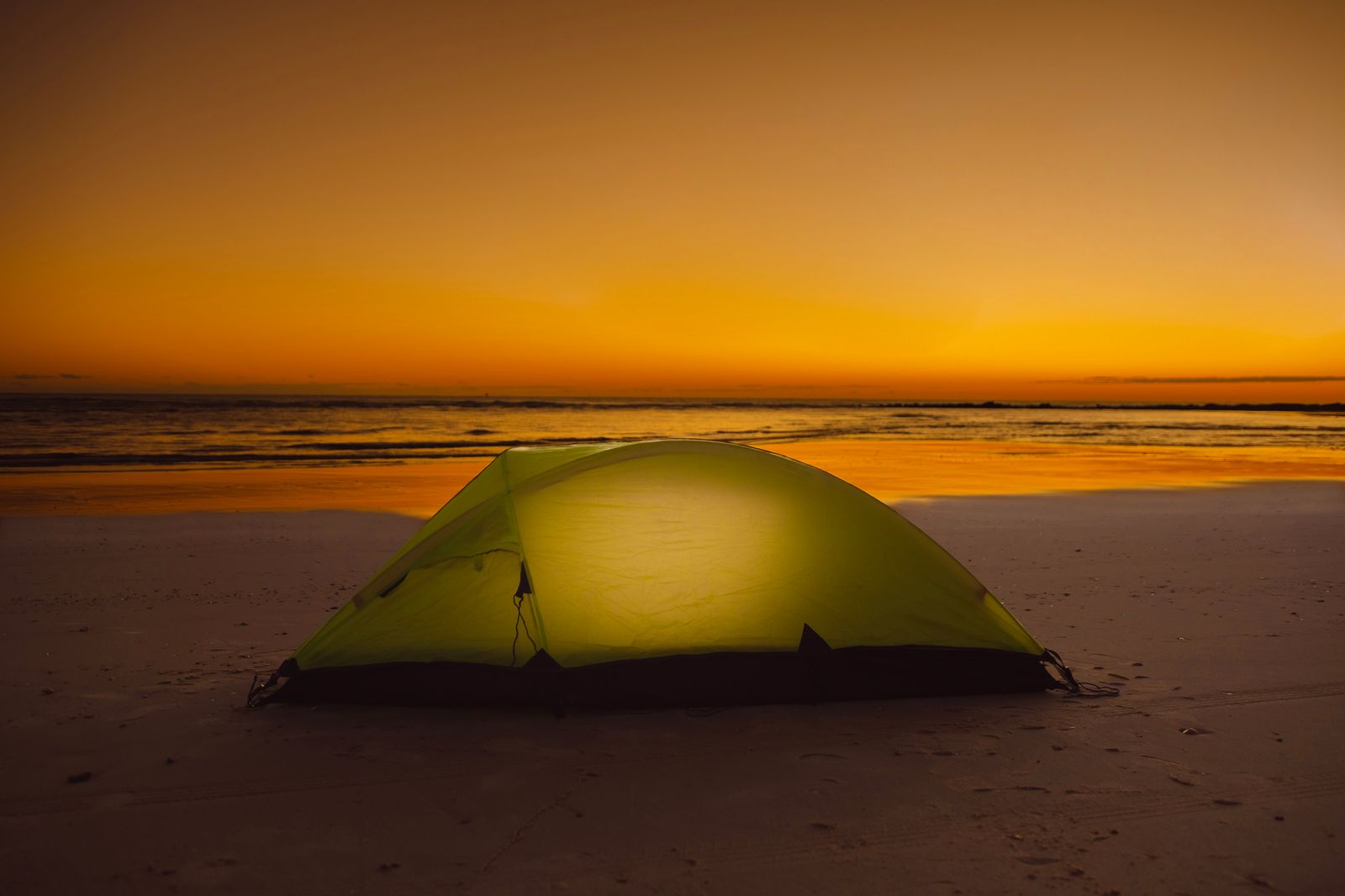 Tente lumineuse installée sur la plage au coucher du soleil