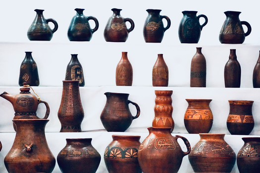 A collection of handmade clay pottery displayed on shelves at a museum exhibition.