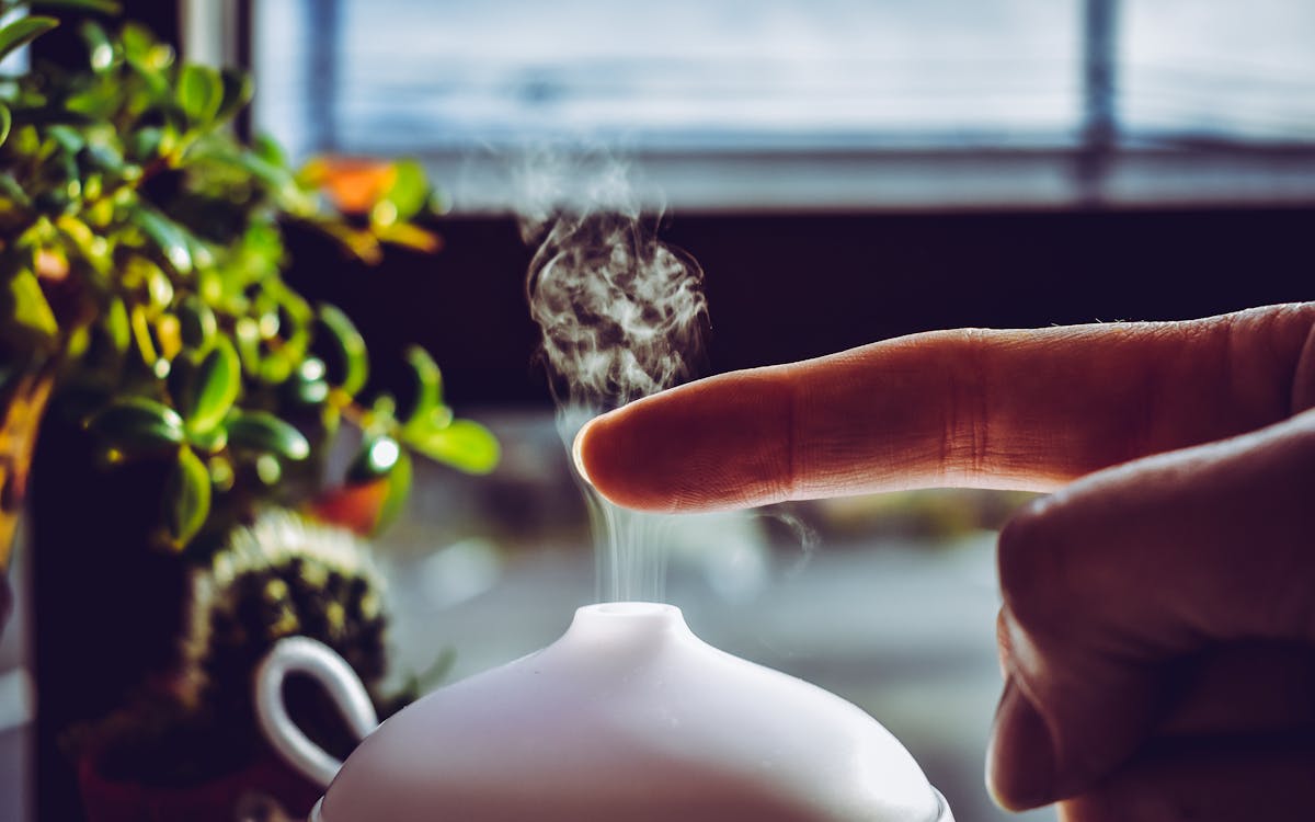 A hand touches mist rising from a diffuser, creating a relaxing ambiance indoors.