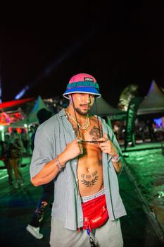 Man wearing a stylish bucket hat and red bag at a vibrant night event.