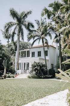 Elegant mansion surrounded by lush gardens and palm trees under the sun.