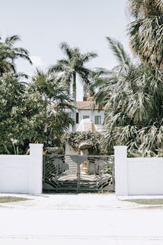 A luxurious villa with tropical palm trees and a decorative iron gate, exuding elegance.