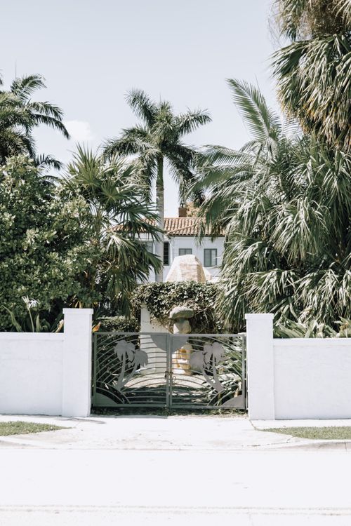 Free A luxurious villa with tropical palm trees and a decorative iron gate, exuding elegance. Stock Photo