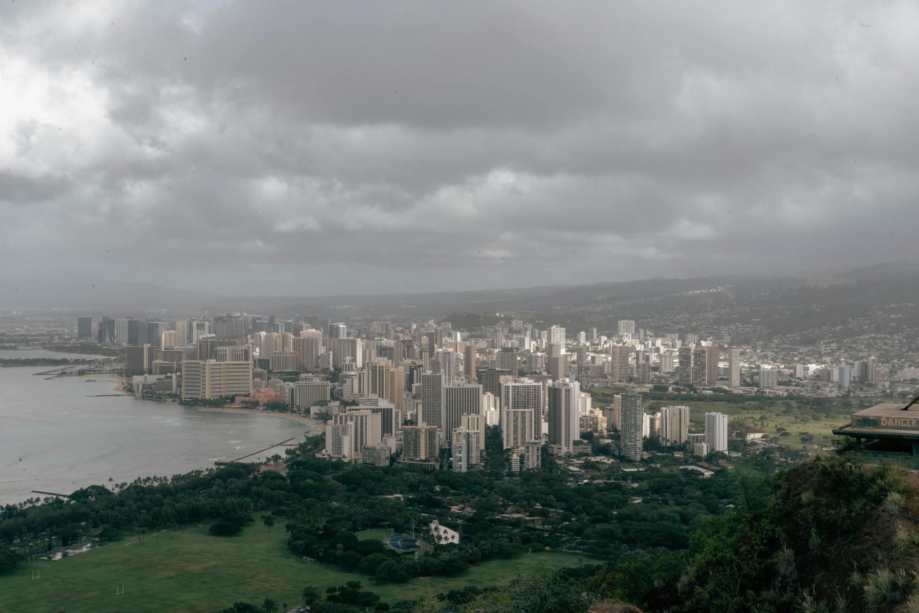 Photo by David Yu Aerial view of Honolulu's skyline with overcast skies, capturing urban skyscrapers and coastal scenery.