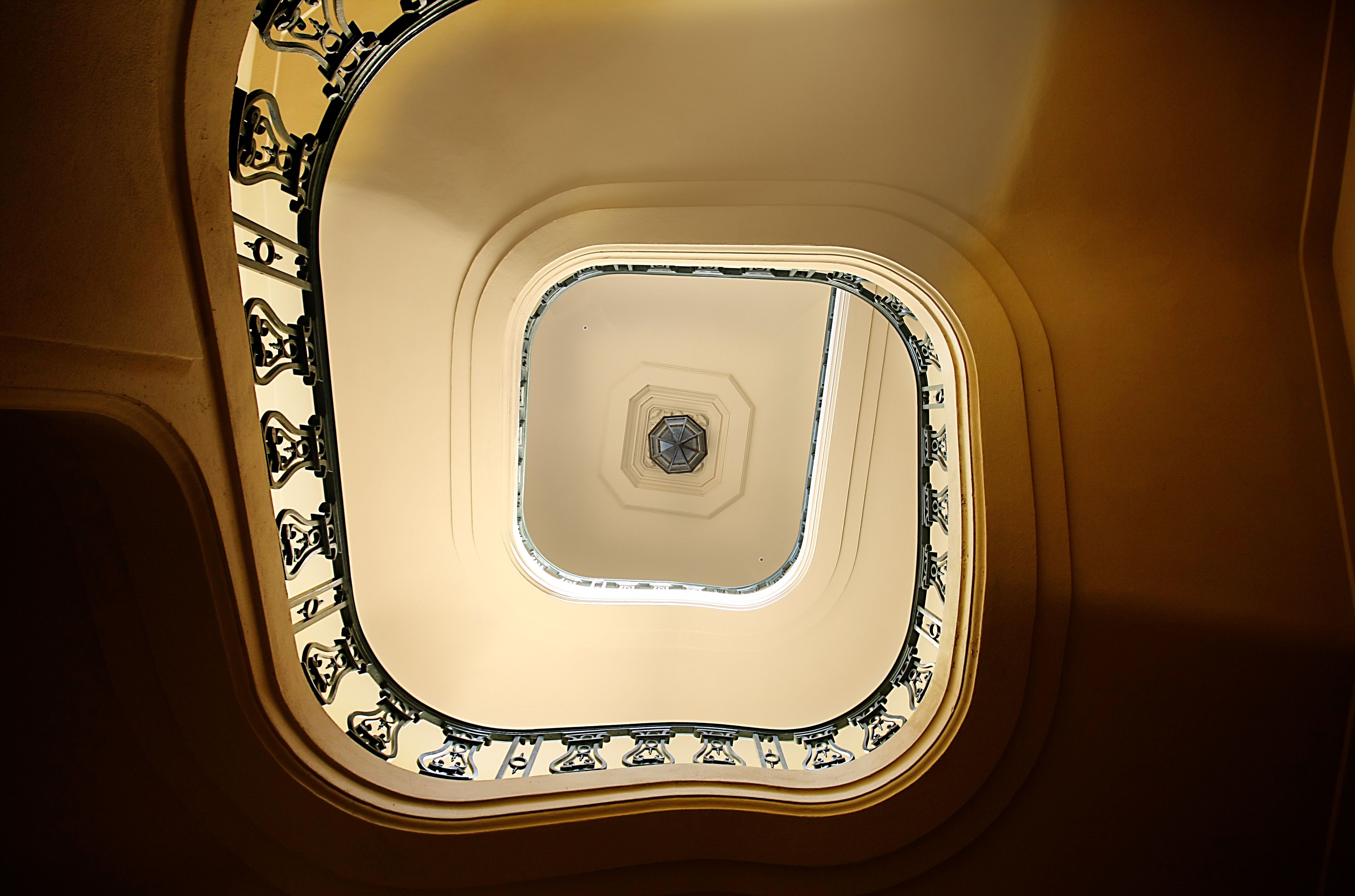 Looking up the center of a beautifully designed spiral staircase with artistic railings and a skylight.