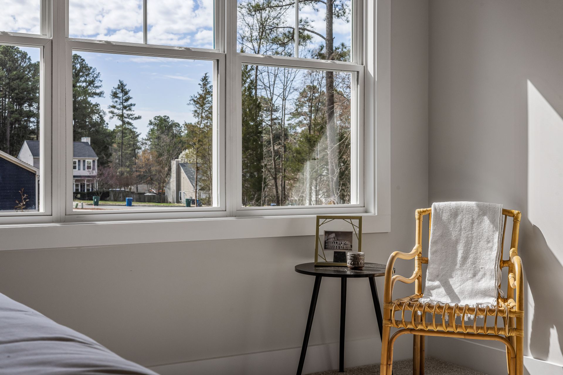 A cozy bedroom interior with a chair and a view of suburban homes through a large window.