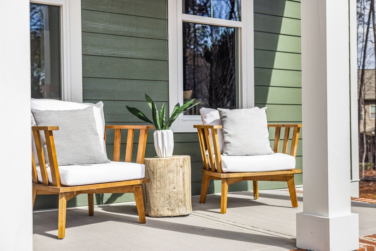 Porch with wooden armchairs and a potted plant against green siding