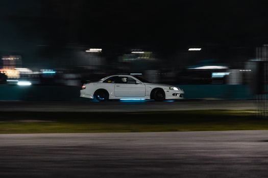Dynamic shot of a white drift car racing at night, showcasing motion and speed.