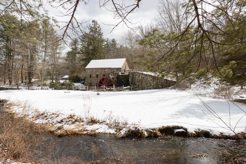 Free A charming rustic stone mill surrounded by snow and a serene stream in a winter forest. Stock Photo