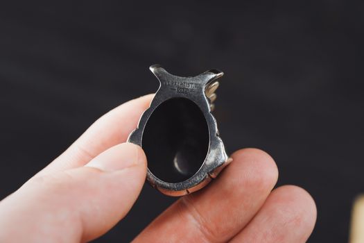 Detailed close-up image of a hand holding a unique silver ring against a black background.