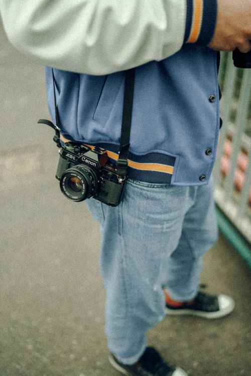Free Person wearing a blue jacket and jeans with a vintage camera, standing outdoors. Stock Photo