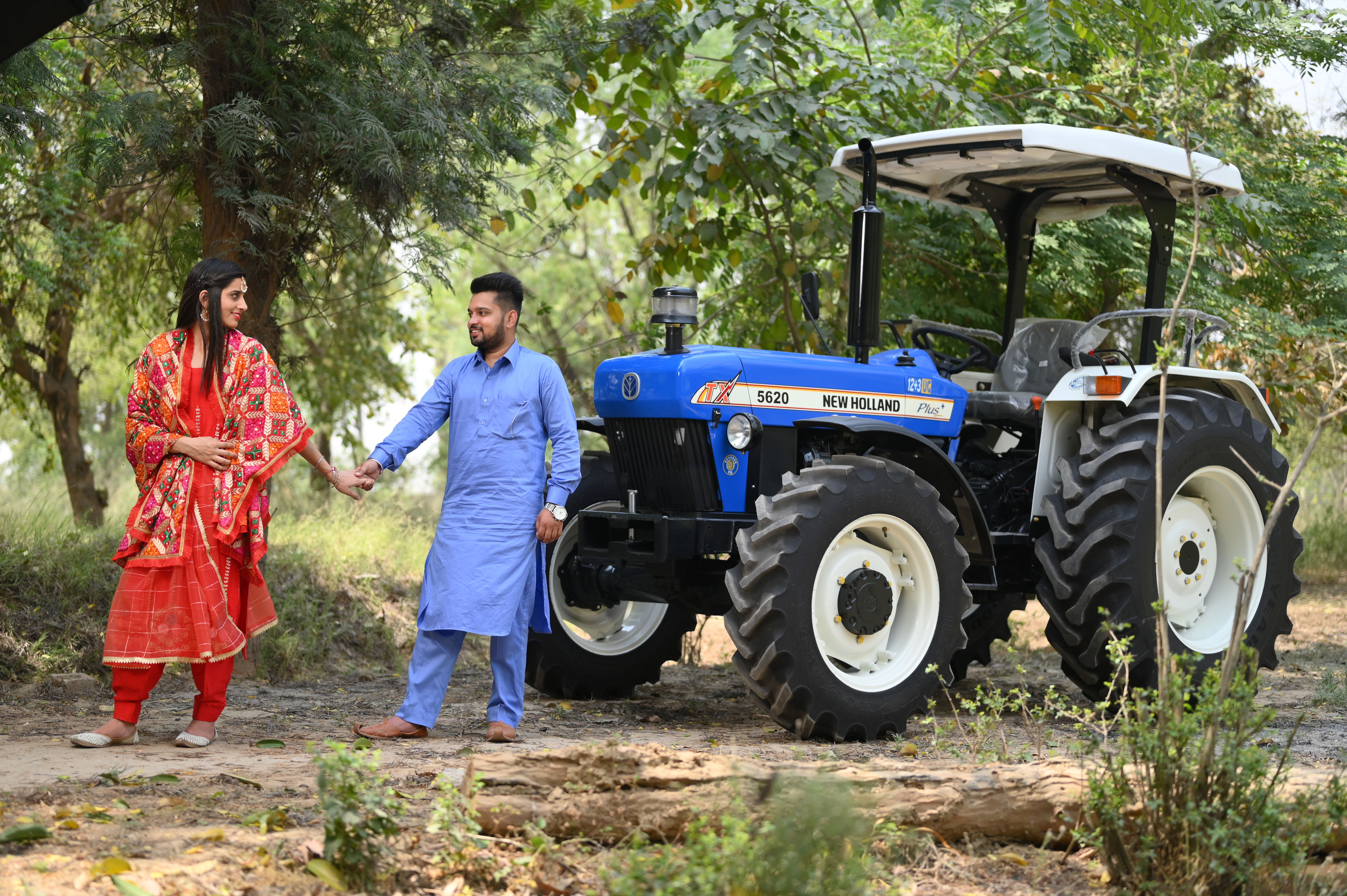 A couple in traditional attire holding hands by a tractor in rural Punjab, India.