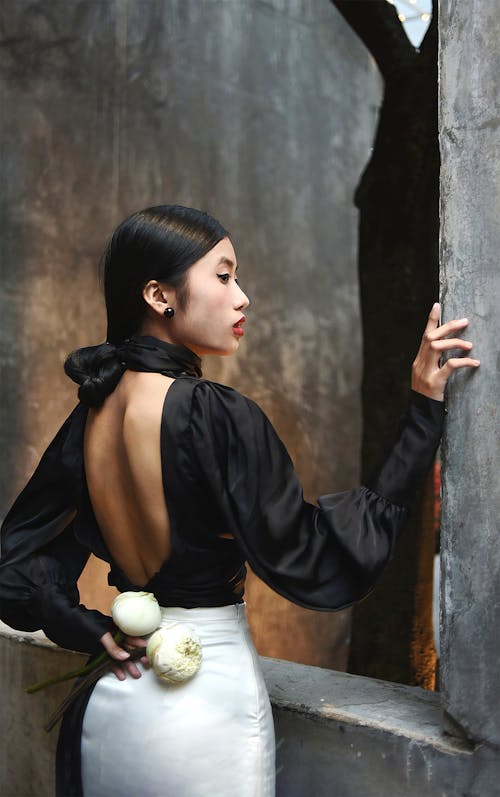 Woman Posing in a Black Blouse with Back Decollete by a Concrete Wall