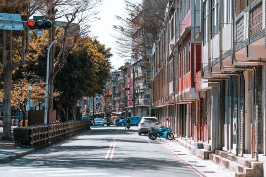 A quiet urban street scene featuring trees, parked motorbike, and buildings under a sunny sky.