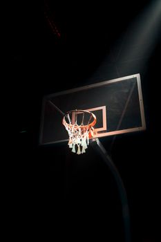 Moody image of a basketball hoop under spotlight capturing the essence of the game.