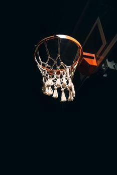 An upward view of a basketball hoop illuminated against a dark night sky, showcasing the hoop and net.
