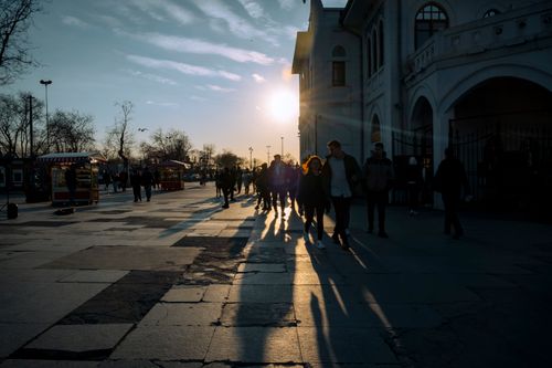 Free Silhouetted pedestrians walking in the city at sunset, casting long shadows on the pavement. Stock Photo
