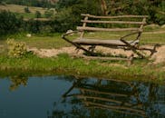 质朴的木凳俯瞰着宁静池塘的清晰倒影，坐落在郁郁葱葱的户外环境中