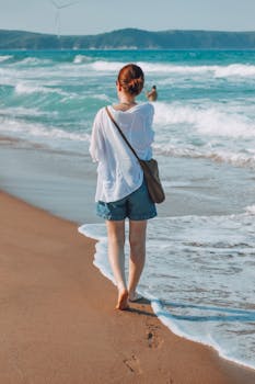Woman walking along the beach with waves gently lapping at her feet on a sunny day.