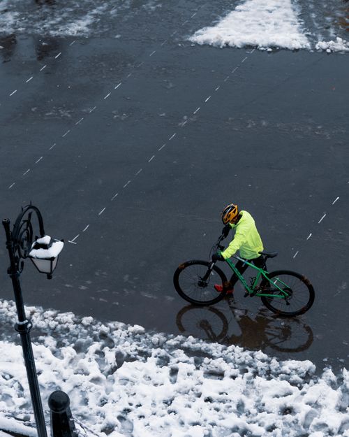 Free A cyclist in bright clothing rides through a snowy urban landscape, reflecting winter weather. Stock Photo