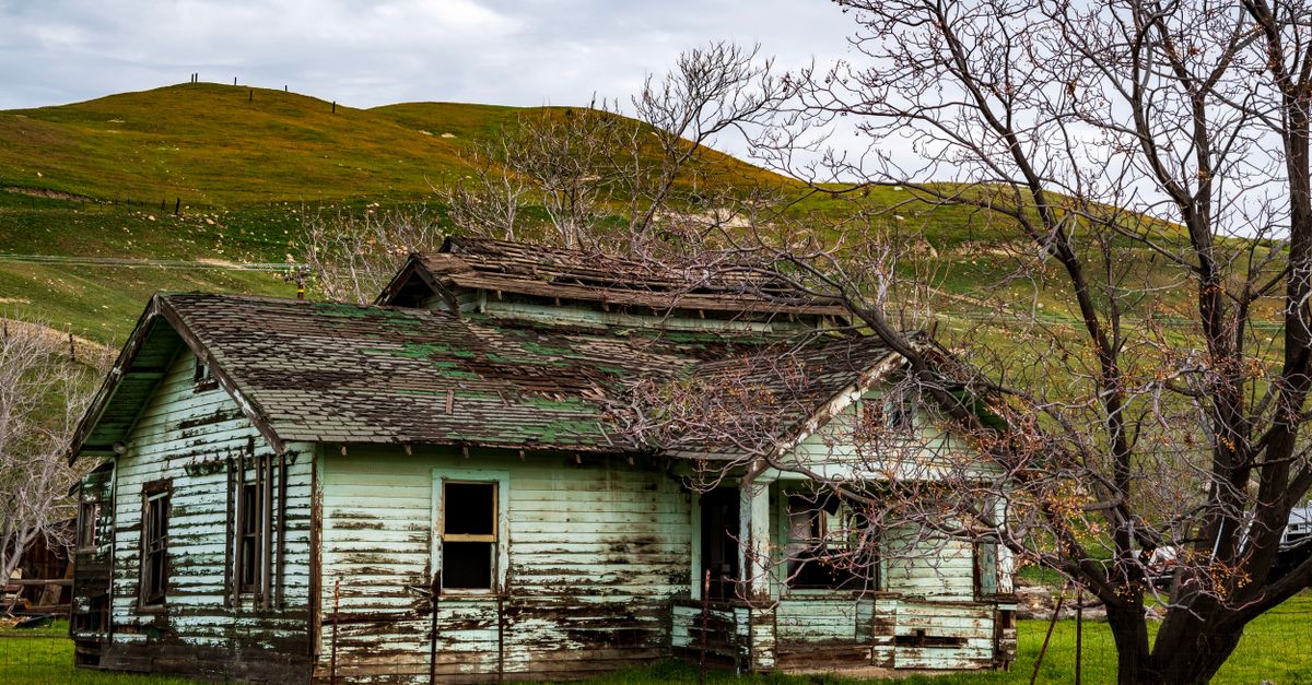 Old, weathered farmhouse amidst hilly rural landscape in Tehachapi, California.