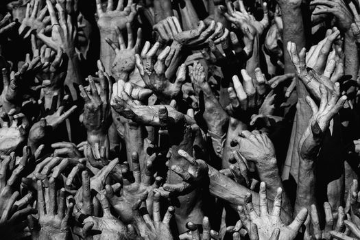 Dramatic black and white photo of numerous clay hands reaching upward.