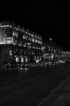 Black and white photo of a city street at night with illuminated buildings and traffic.