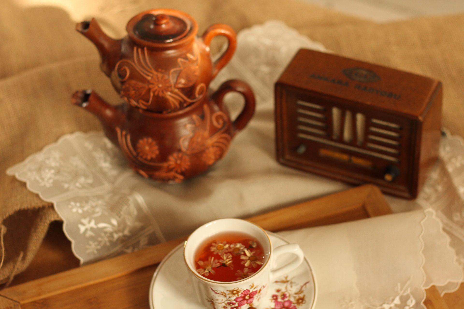 A cozy still life featuring a vintage tea set and antique radio on a lace tablecloth.
