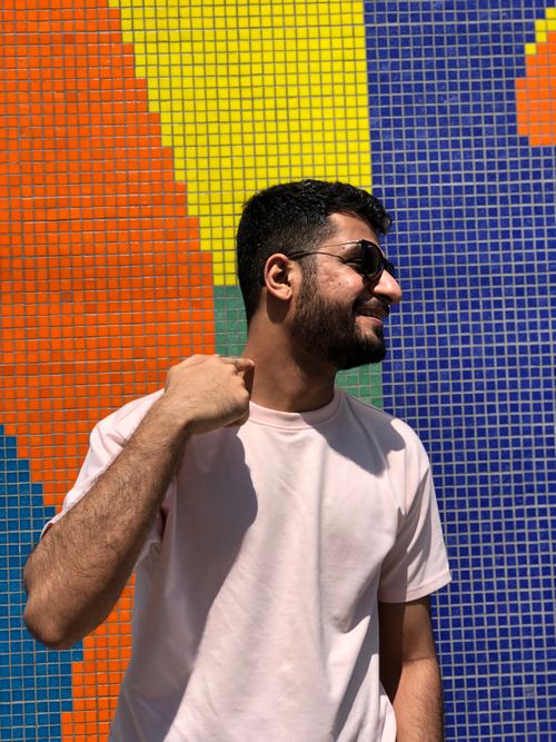 Free Young man in sunglasses posing against a colorful mosaic wall, enjoying a sunlit day. Stock Photo
