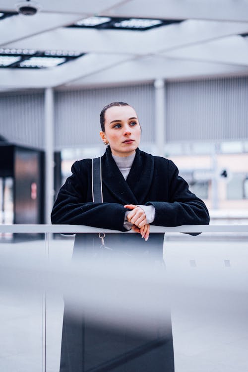 Woman in a Black Coat Standing and Leaning on a Railing 